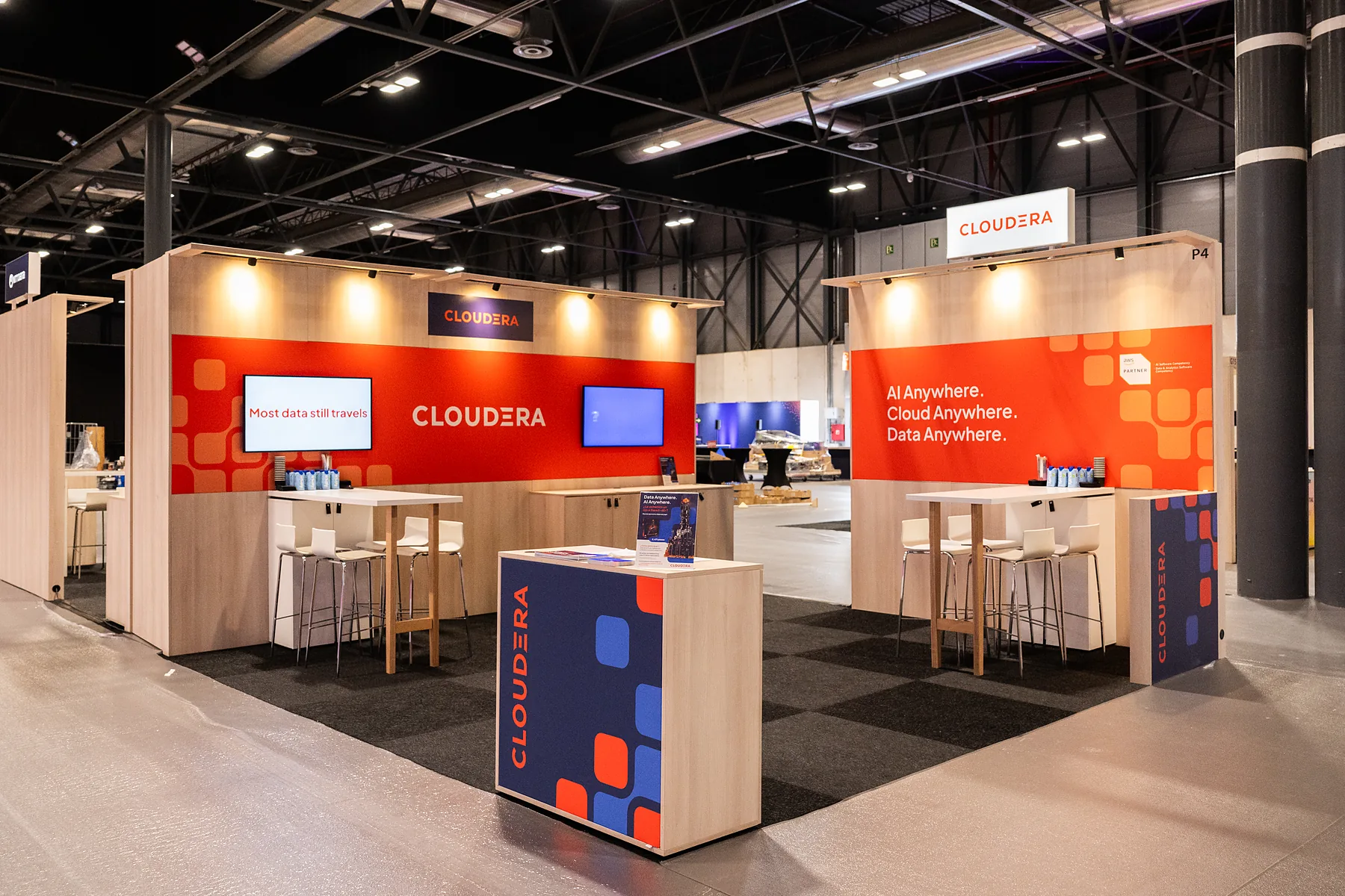 Stand van Cloudera met oranje printwanden, een scherm en een balie met logo op de beursvloer