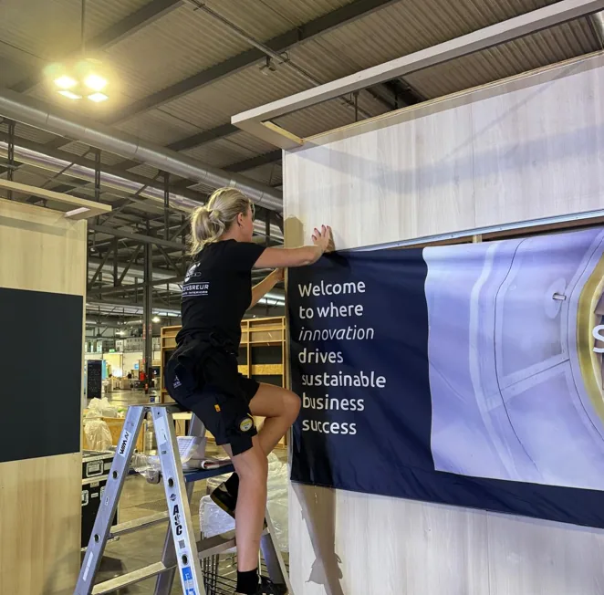 Fitter on a ladder applying a printed banner to the stand wall
