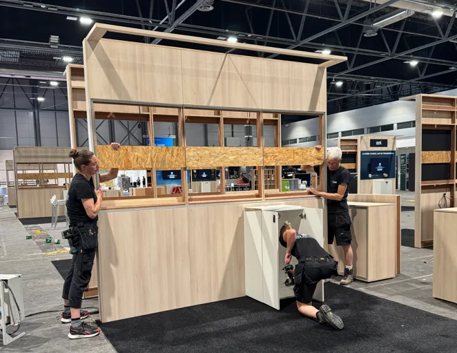 Three fitters setting up a birch wall with cabinets on the exhibition floor