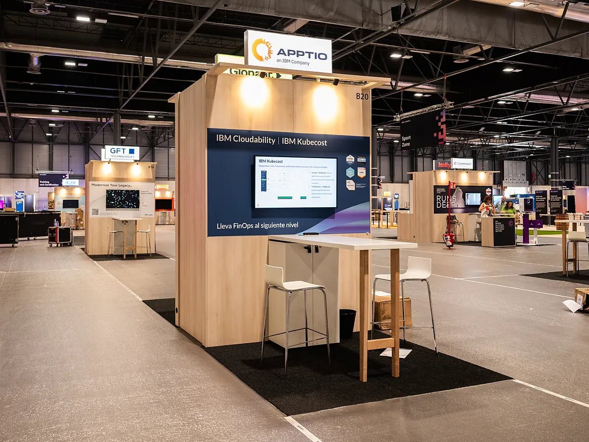 Apptio stand with a dark blue print wall about IBM Cloudability, a screen and a high table with stools