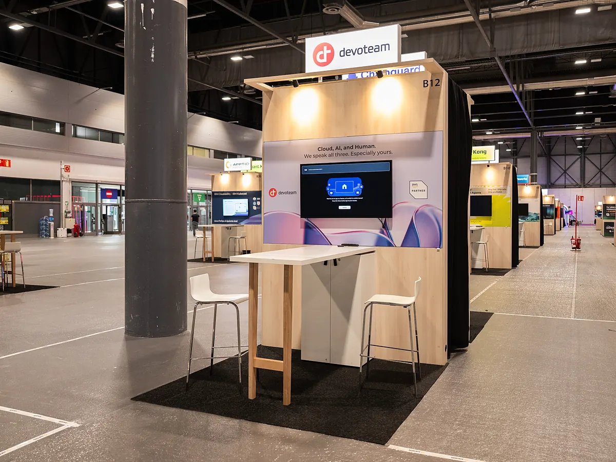 Devoteam stand with a blue print wall, a screen and a high table with stools