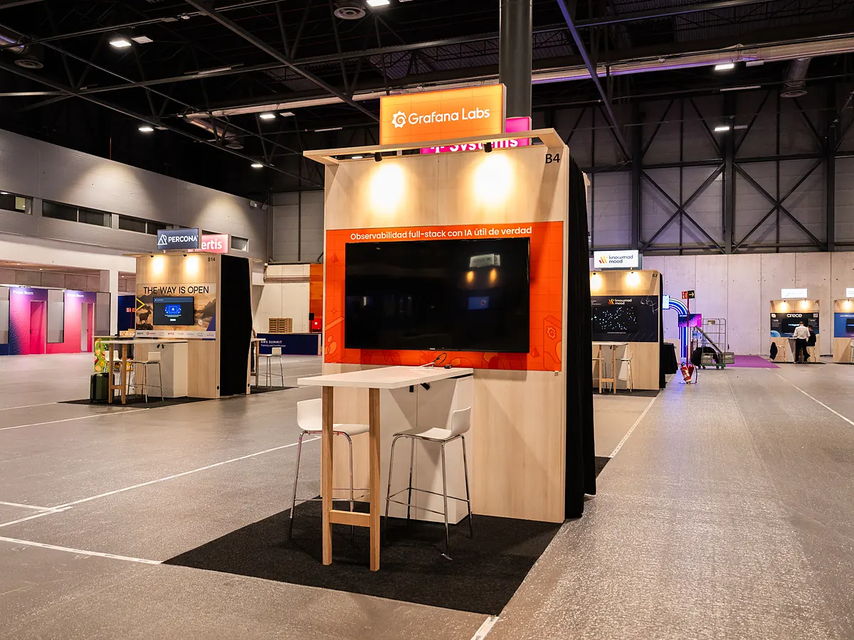 Grafana Labs stand with an orange print wall, a screen and a high table with stools
