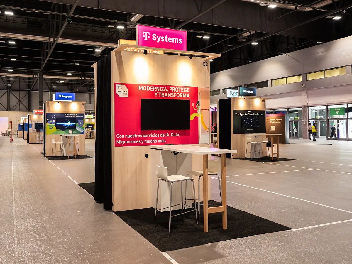 T-Systems stand with a magenta print wall, a screen and a high table with stools