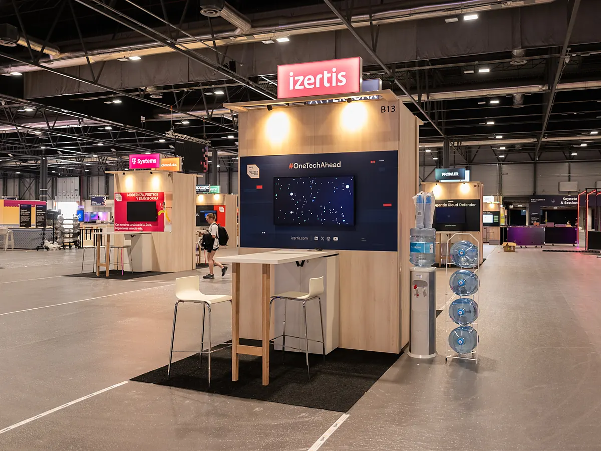 Izertis stand with a dark blue print wall, a screen, a high table and a water dispenser