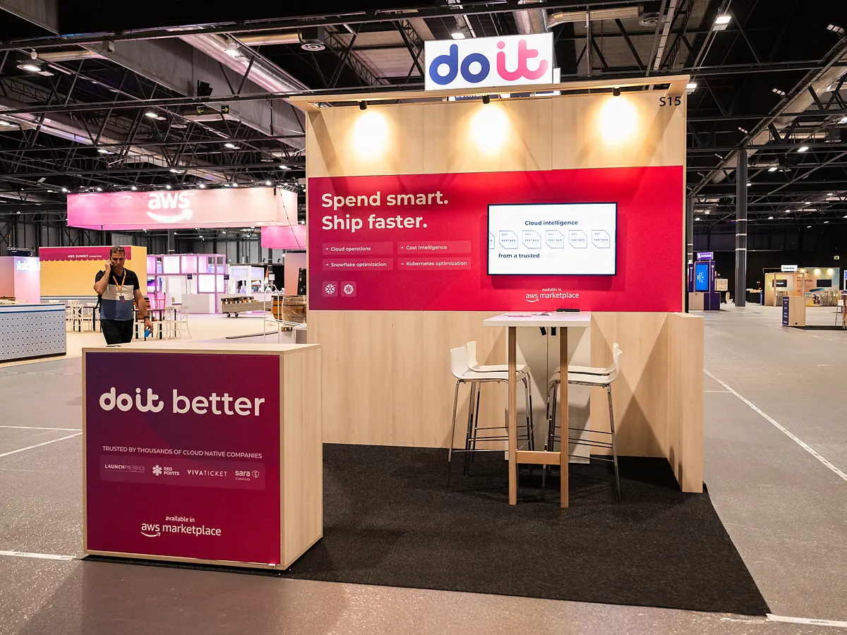 DoiT stand with a red print wall, a screen, a high table with stools and a counter with the logo