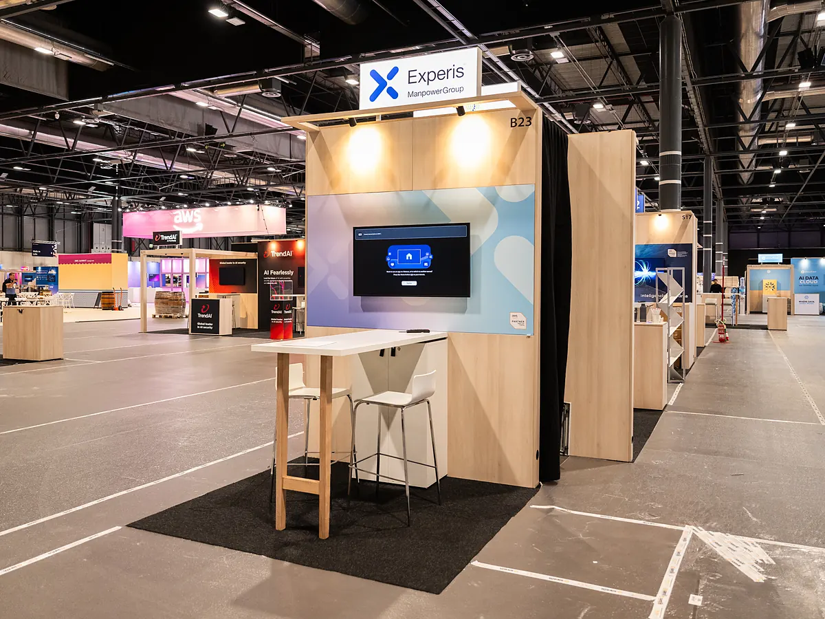 Experis stand with a light blue print wall, a screen and a high table with stools