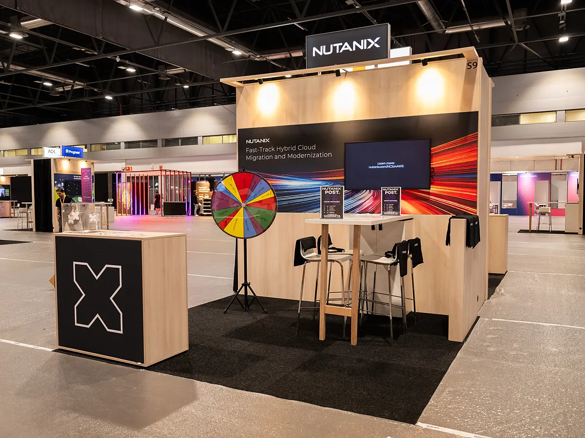 Nutanix stand with a dark print wall, a screen, a prize wheel and a counter with the logo