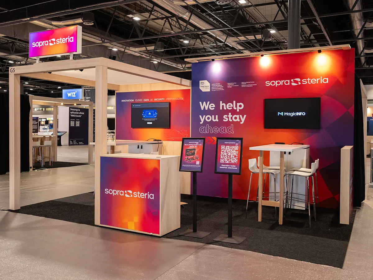 Sopra Steria stand with a red and purple print wall, a screen, a counter with the logo and a high table with stools