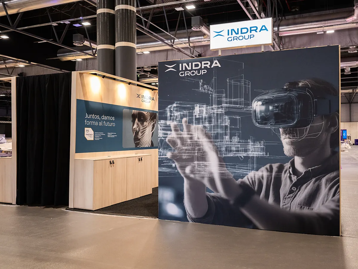Indra Group corner stand with a large print of a man wearing a VR headset and a wall of cabinets