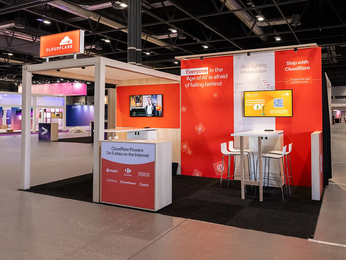 Cloudflare stand with an orange print wall, an illuminated logo box above the portal and a counter showing partner logos