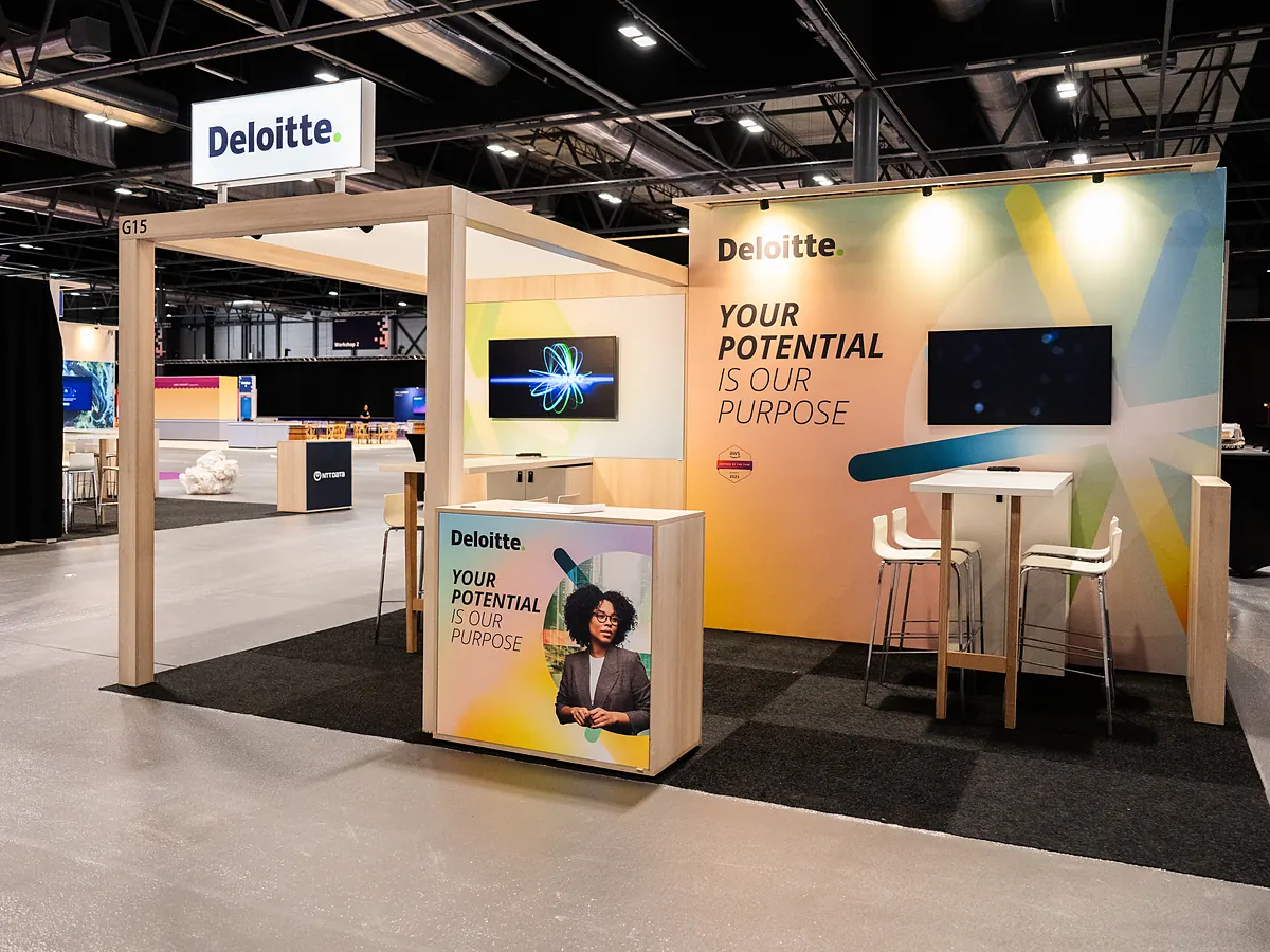 Deloitte corner stand with an open portal, a print wall in light colours, two screens and a counter with a photo