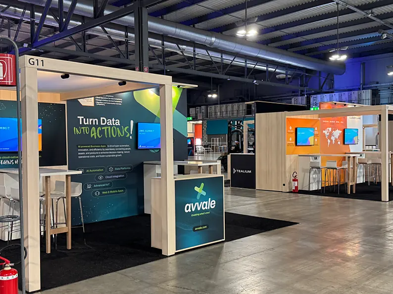 Avvale stand with an open portal, a green print wall with a screen and a counter with the logo