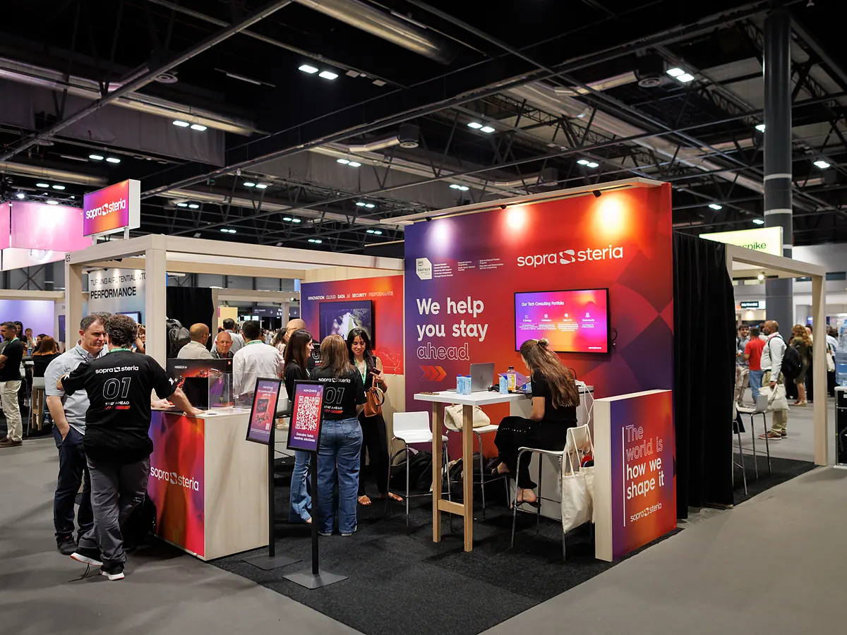 Sopra Steria stand on a busy exhibition floor, with visitors at the counter and the high table